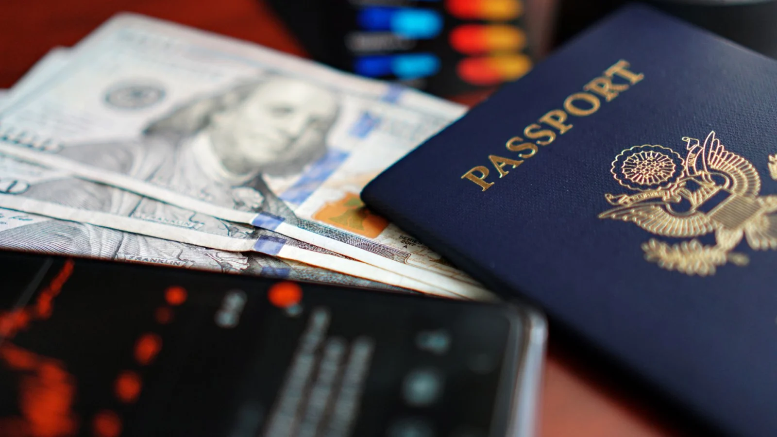 A close-up image of a U.S. passport, dollar bills, and a smartphone.